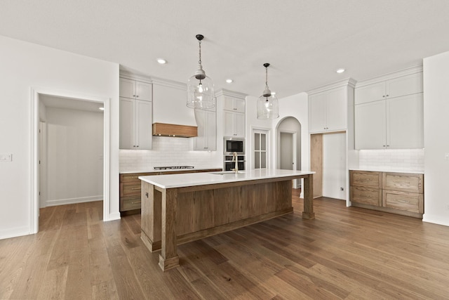 kitchen with a spacious island, built in microwave, hanging light fixtures, white cabinets, and sink