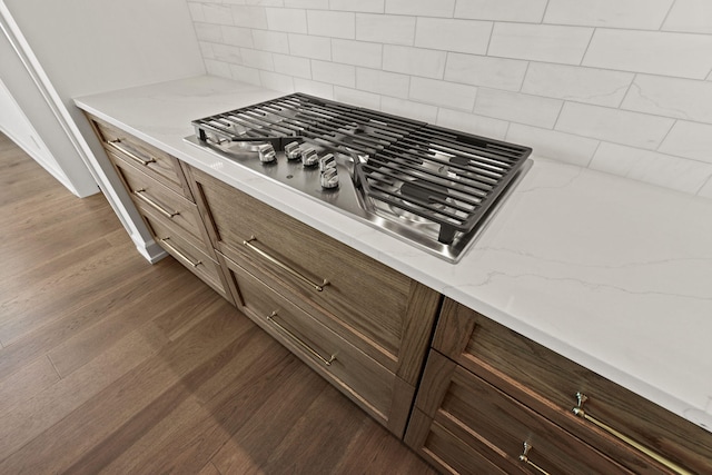 details with decorative backsplash, light stone counters, dark hardwood / wood-style flooring, and stainless steel gas cooktop