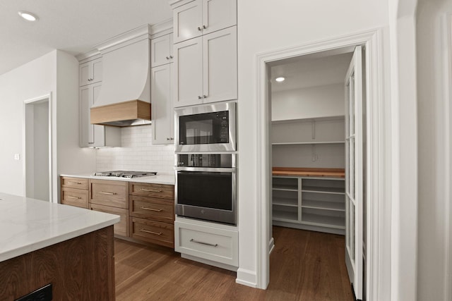 kitchen with white cabinetry, custom exhaust hood, backsplash, stainless steel gas cooktop, and light stone countertops