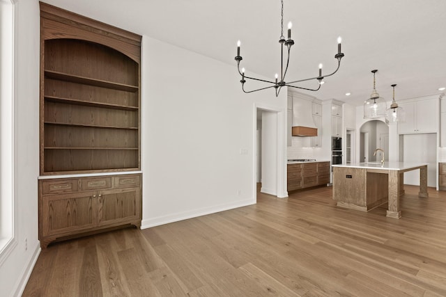 kitchen featuring light hardwood / wood-style floors, a center island with sink, cooktop, white cabinetry, and hanging light fixtures