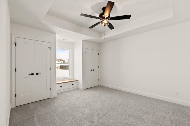 unfurnished bedroom with ceiling fan, light colored carpet, and a raised ceiling