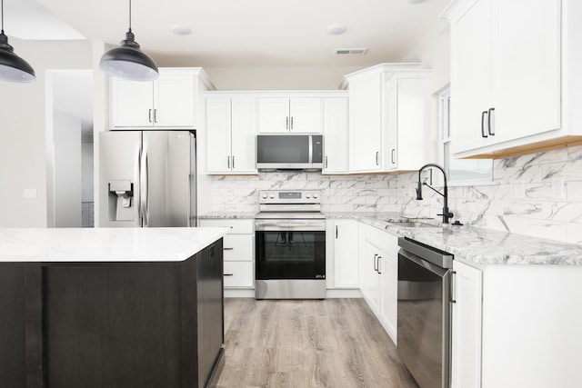 kitchen featuring light wood-style flooring, decorative backsplash, appliances with stainless steel finishes, white cabinets, and a sink