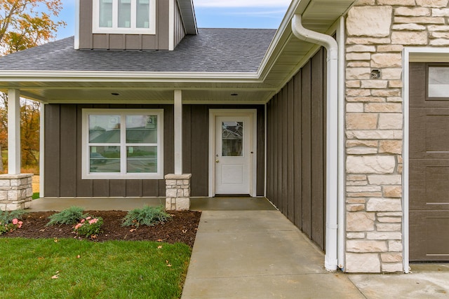 entrance to property featuring a garage, stone siding, a shingled roof, and board and batten siding