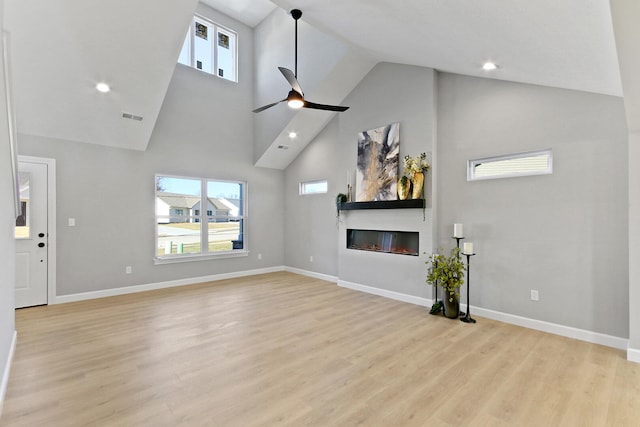 unfurnished living room with light wood-type flooring, a glass covered fireplace, visible vents, and a healthy amount of sunlight