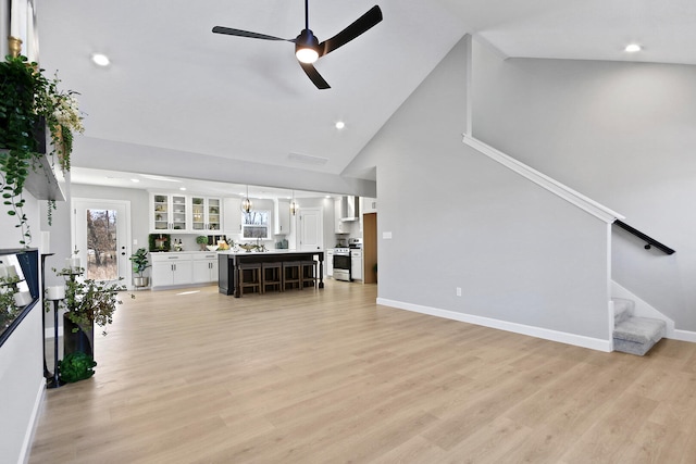 living area with light wood-type flooring, ceiling fan, stairway, and baseboards