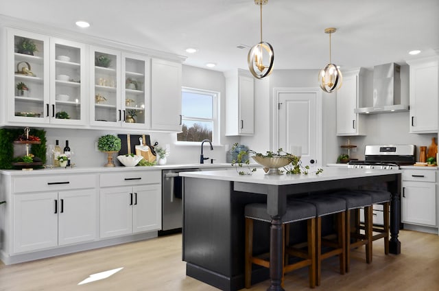 kitchen featuring wall chimney exhaust hood, a kitchen island, appliances with stainless steel finishes, a kitchen bar, and white cabinetry