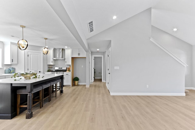 kitchen featuring visible vents, white cabinets, light countertops, wall chimney exhaust hood, and gas range