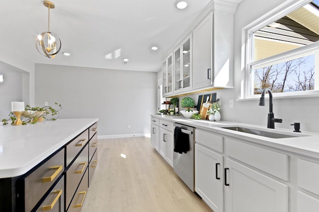 kitchen featuring light countertops, light wood-style flooring, glass insert cabinets, a sink, and dishwasher