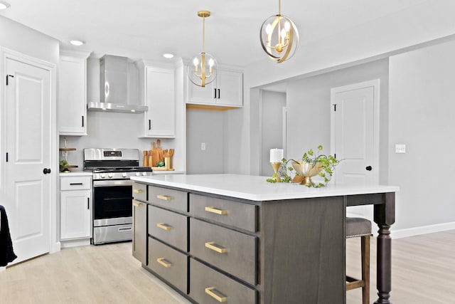 kitchen featuring a kitchen island, light countertops, wall chimney range hood, stainless steel range with gas cooktop, and white cabinetry