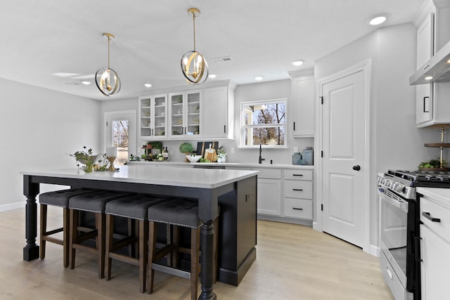 kitchen with white cabinets, wall chimney exhaust hood, a kitchen breakfast bar, and stainless steel range with gas stovetop