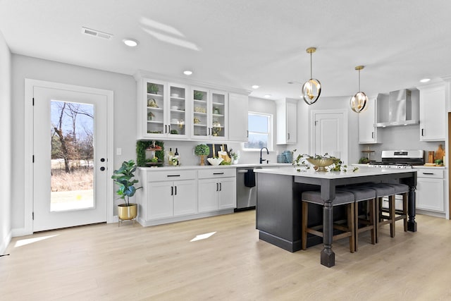 kitchen featuring appliances with stainless steel finishes, white cabinets, visible vents, and wall chimney exhaust hood