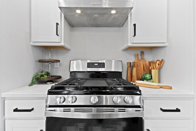 kitchen with stainless steel range with gas cooktop, exhaust hood, light countertops, and white cabinetry