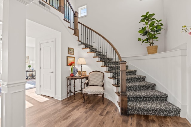 staircase featuring decorative columns, a towering ceiling, and hardwood / wood-style floors