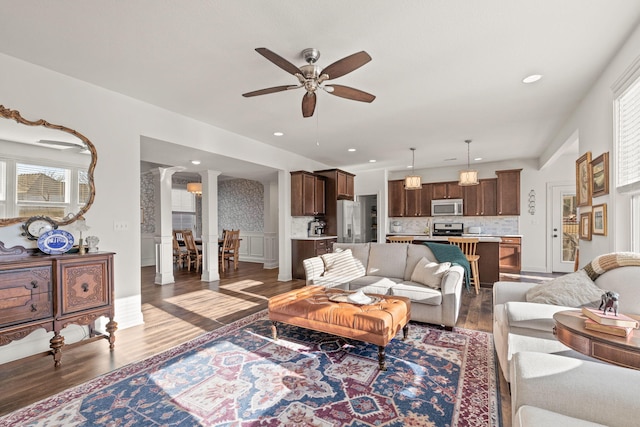 living room with dark wood-type flooring, ceiling fan, and decorative columns