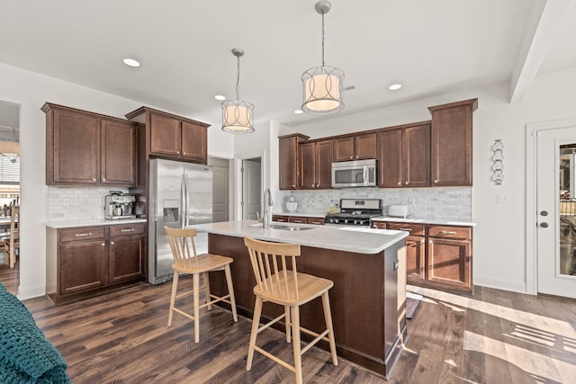 kitchen with sink, hanging light fixtures, a kitchen island with sink, stainless steel appliances, and dark wood-type flooring