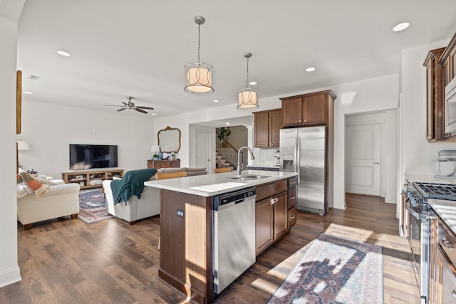 kitchen featuring appliances with stainless steel finishes, decorative light fixtures, sink, backsplash, and a center island with sink