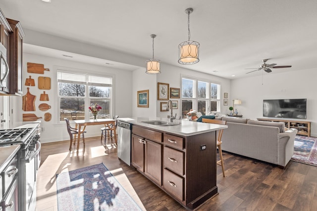 kitchen featuring appliances with stainless steel finishes, decorative light fixtures, sink, dark brown cabinets, and a center island with sink