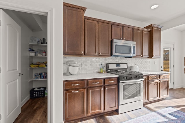 kitchen with tasteful backsplash, appliances with stainless steel finishes, dark wood-type flooring, and dark brown cabinets