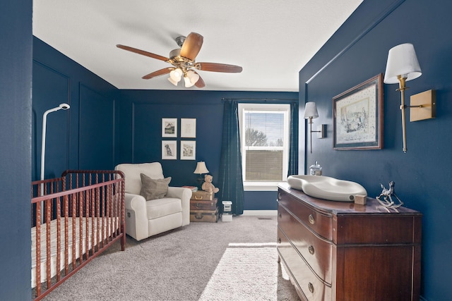 bedroom with a nursery area, ceiling fan, and light colored carpet