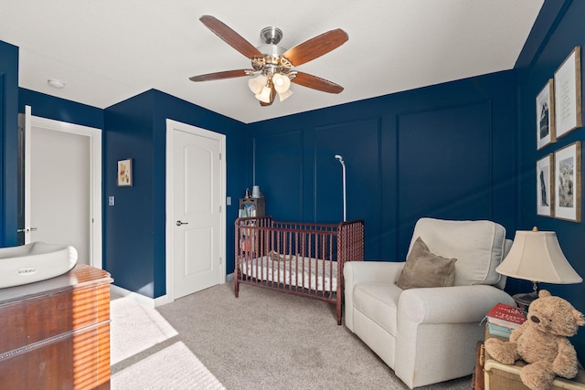 carpeted bedroom featuring a nursery area and ceiling fan