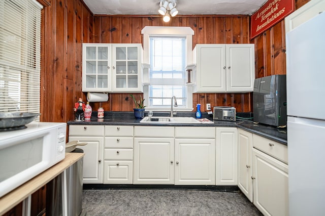 kitchen with wooden walls, white appliances, white cabinetry, and sink