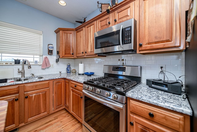 kitchen featuring decorative backsplash, sink, light wood-type flooring, stainless steel appliances, and light stone counters