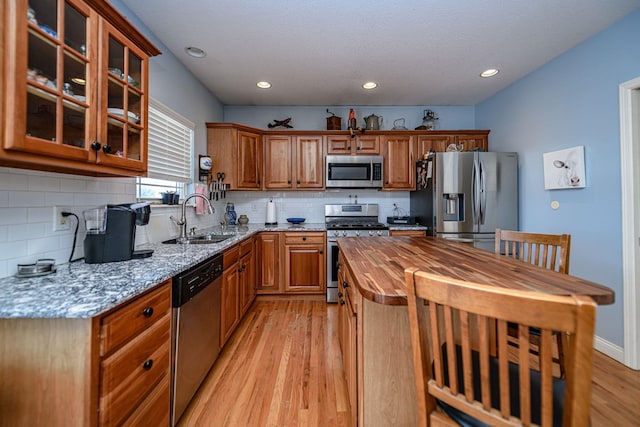 kitchen featuring appliances with stainless steel finishes, sink, light wood-type flooring, light stone counters, and decorative backsplash