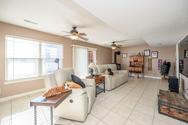 living room with a wood stove, ceiling fan, light tile patterned floors, and a textured ceiling