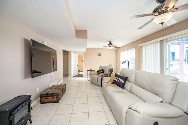 tiled living room with ceiling fan, a wealth of natural light, and a wood stove