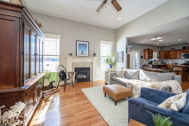 living room with ceiling fan, light hardwood / wood-style flooring, and a tiled fireplace