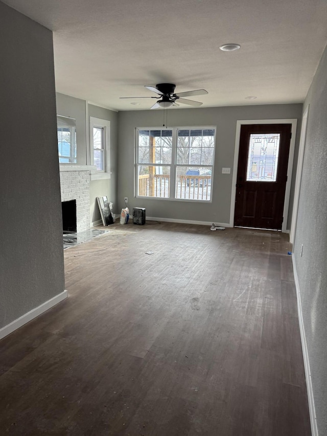 unfurnished living room featuring ceiling fan, dark wood-type flooring, and a fireplace