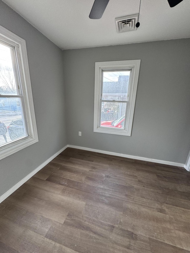 empty room featuring a wealth of natural light, dark wood-type flooring, and ceiling fan