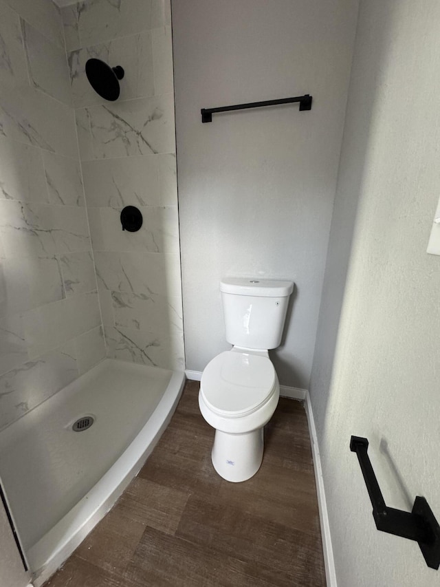 bathroom with wood-type flooring, tiled shower, and toilet