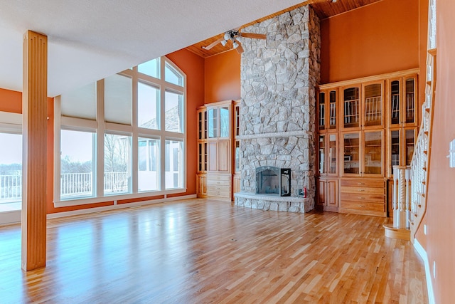 unfurnished living room featuring light wood-type flooring, high vaulted ceiling, a stone fireplace, and wood ceiling