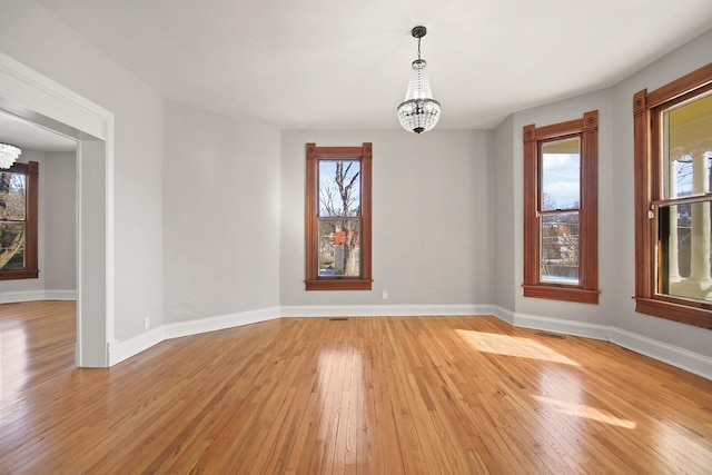 empty room featuring a wealth of natural light, a notable chandelier, and light hardwood / wood-style floors