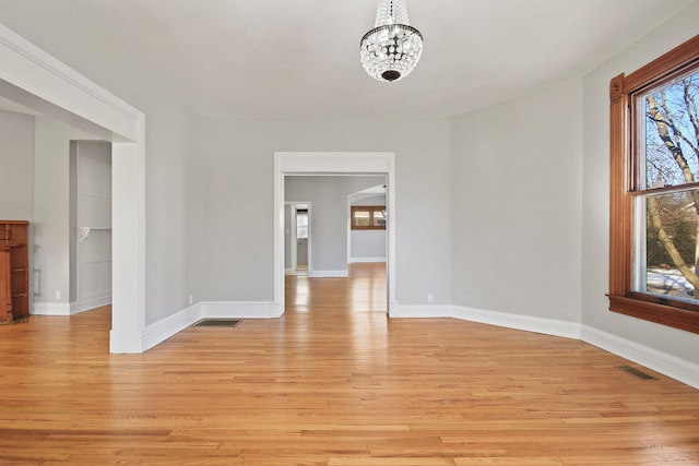 spare room with plenty of natural light, a chandelier, and light hardwood / wood-style floors