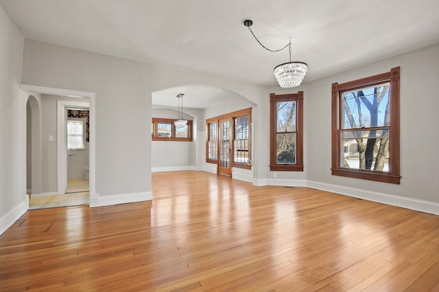 unfurnished living room with an inviting chandelier, a wealth of natural light, and light wood-type flooring