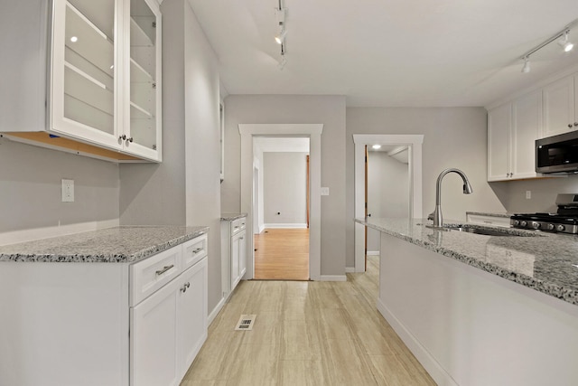 kitchen with rail lighting, sink, white cabinets, light stone counters, and stainless steel appliances