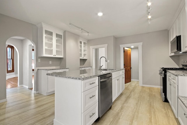 kitchen with an island with sink, sink, white cabinets, stainless steel appliances, and light stone countertops