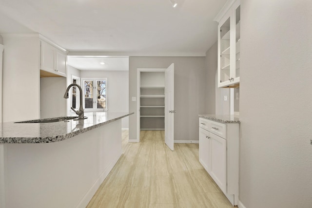 kitchen with white cabinetry, light stone countertops, sink, and light wood-type flooring