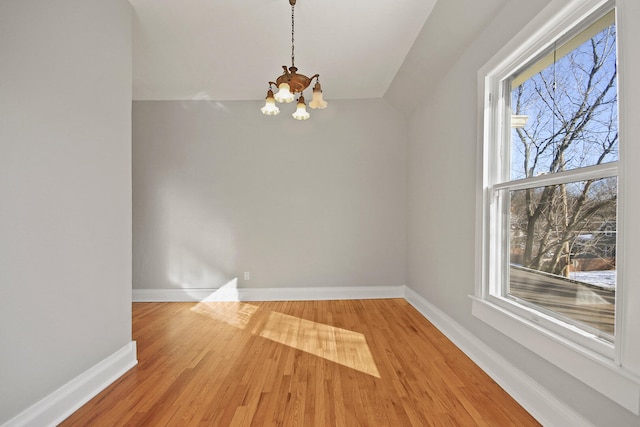 unfurnished dining area featuring hardwood / wood-style flooring, vaulted ceiling, a chandelier, and a healthy amount of sunlight