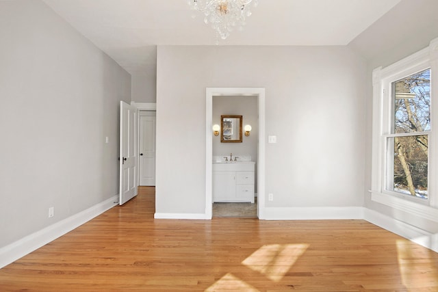 unfurnished bedroom with ensuite bathroom, sink, light hardwood / wood-style floors, and a notable chandelier