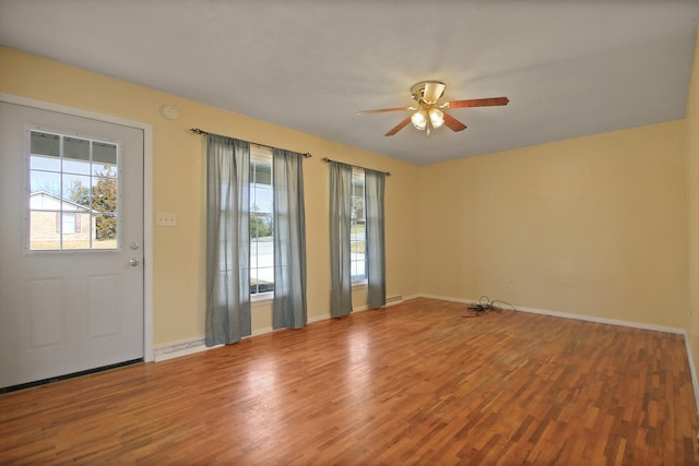 unfurnished room featuring ceiling fan, wood finished floors, a wealth of natural light, and baseboards