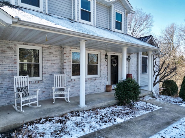 entrance to property featuring a porch and brick siding