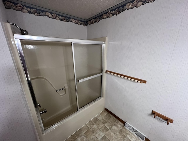 bathroom featuring bath / shower combo with glass door and a textured ceiling