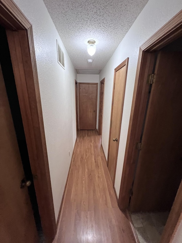 hallway with light hardwood / wood-style flooring and a textured ceiling