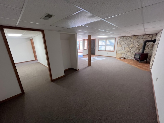 basement featuring a paneled ceiling, carpet floors, and a wood stove