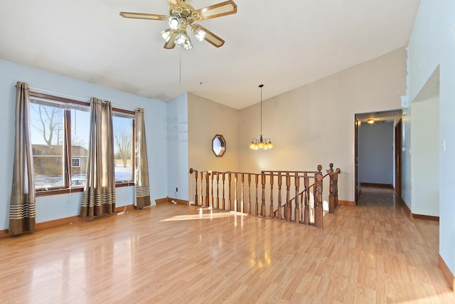 empty room with lofted ceiling, ceiling fan with notable chandelier, and light wood-type flooring