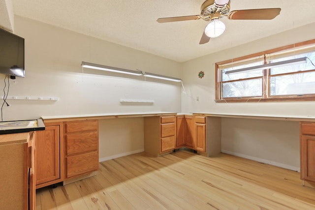 unfurnished office featuring ceiling fan, built in desk, light hardwood / wood-style floors, and a textured ceiling