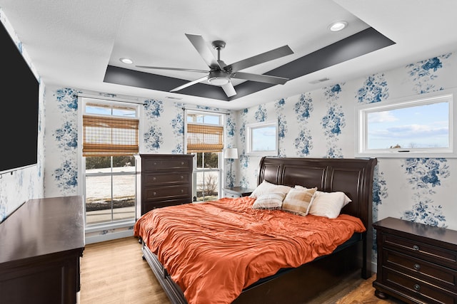 bedroom featuring a raised ceiling, ceiling fan, and light hardwood / wood-style floors